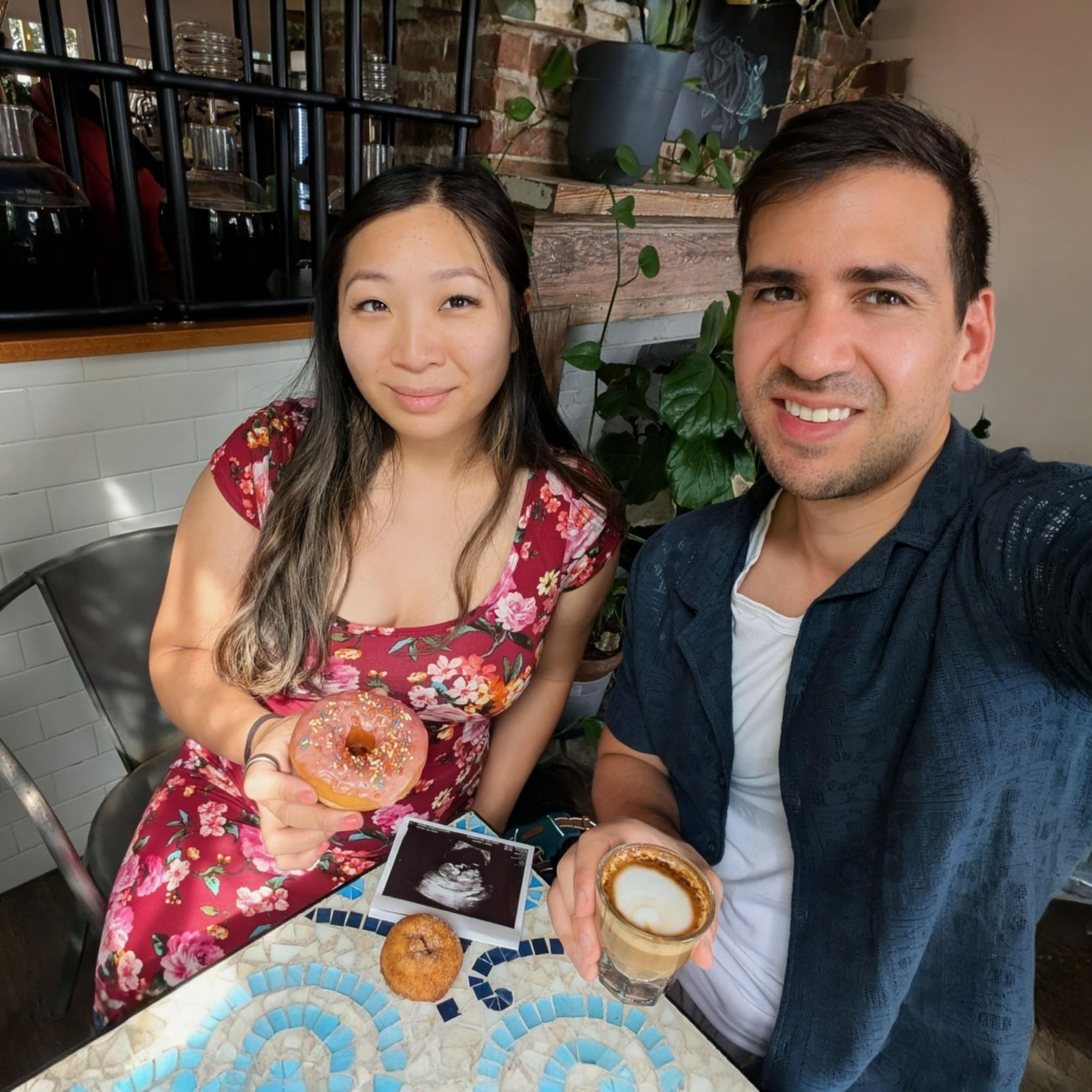 David is holding a macchiato cup and Jenny holding a donut with a photo of an ultrasound on the table